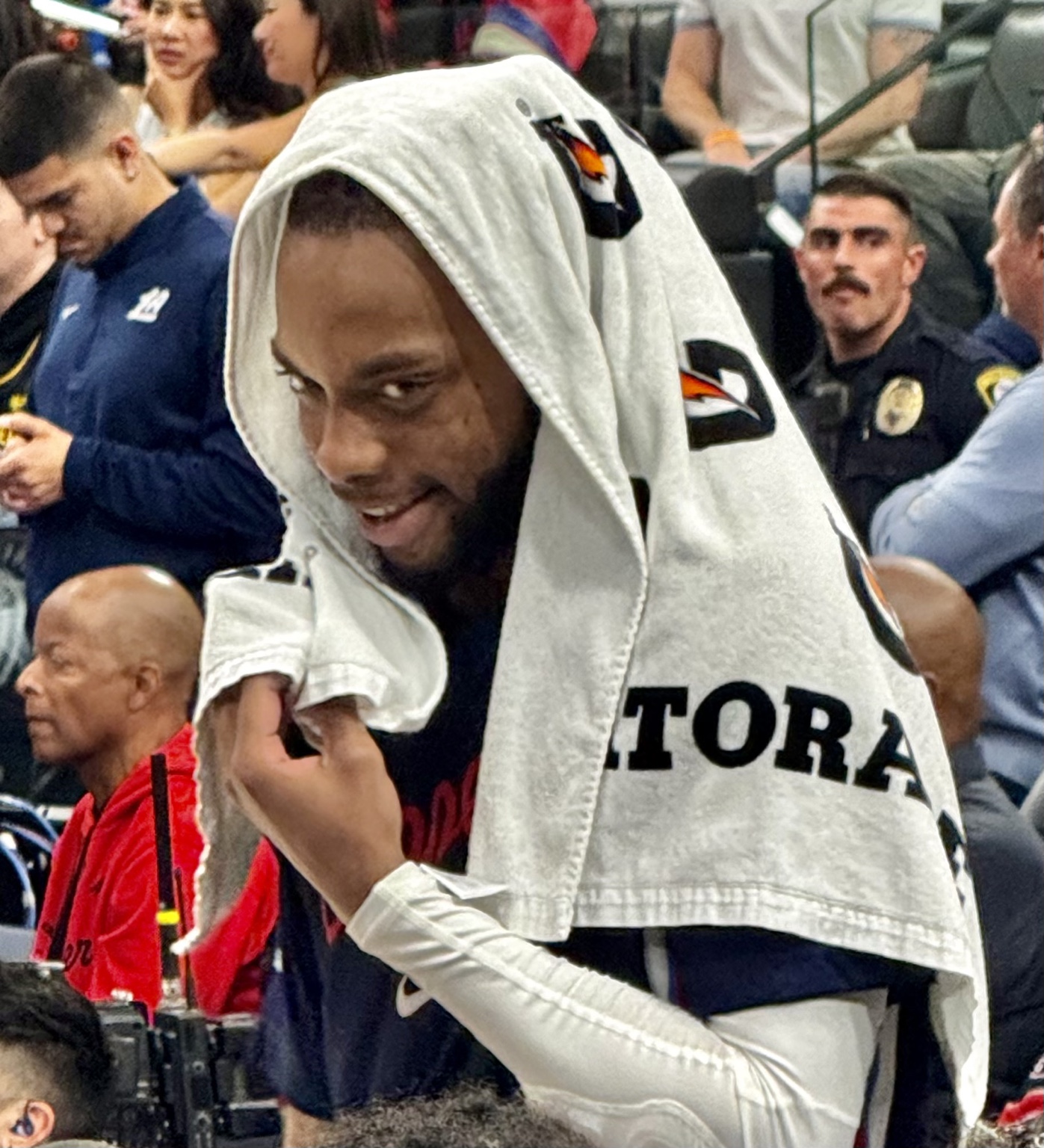 A candid courtside close-up with a basketball player wearing a towel over his head